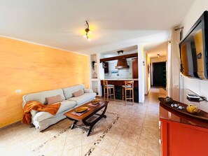 A living room with a sofa, coffee table, and kitchen area with bar stools.