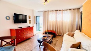 Een woonkamer met een televisie, een rode kast, een beige bank en een eettafel.
