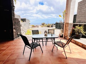 En udendørs patio med et bord og stole, stenvægge og havudsigt.