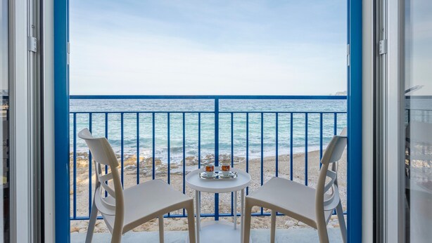 Un balcón con vista al mar, dos sillas y una mesita con tazas.