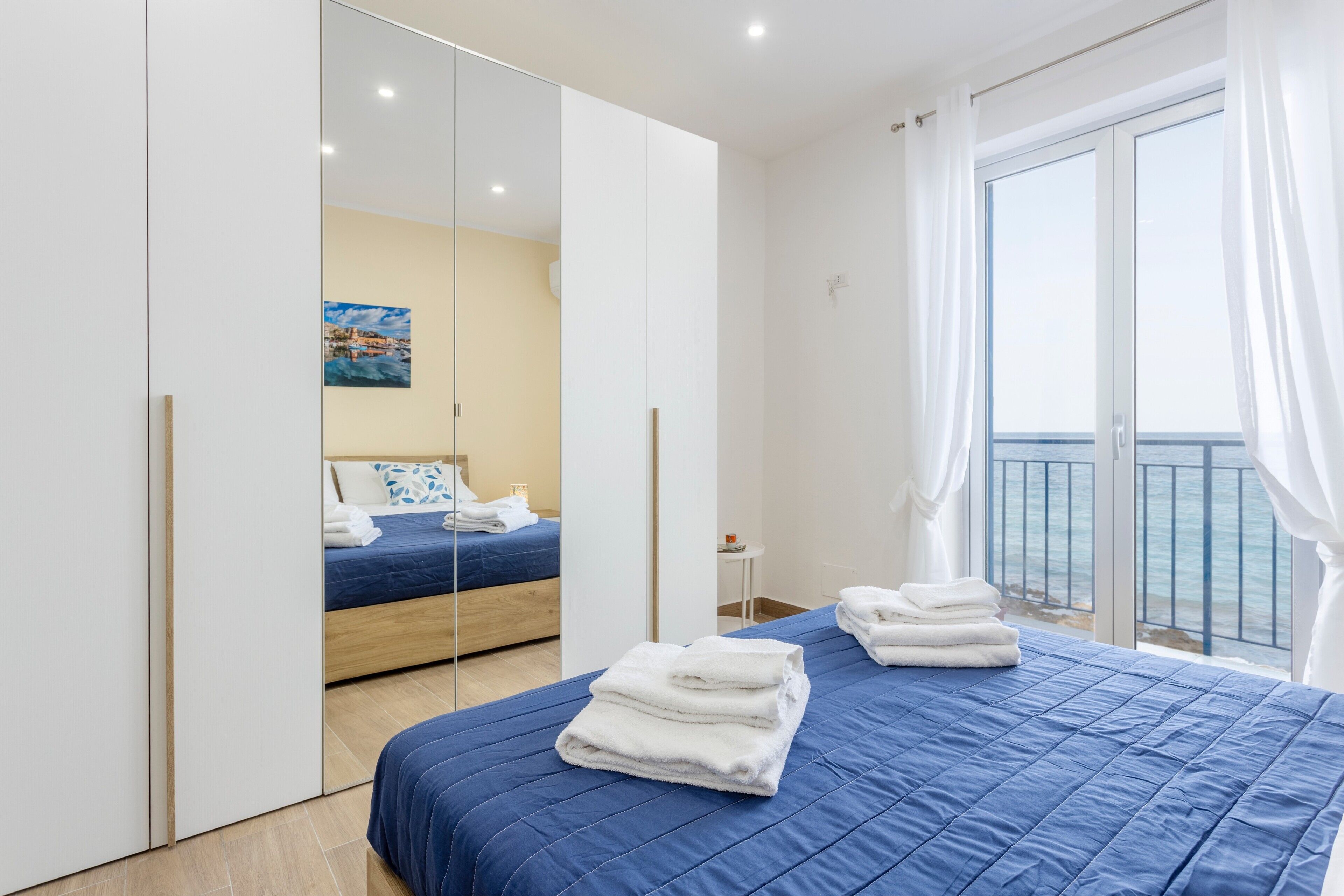 A modern hotel room with a large bed, a balcony with a view, and a large mirror.