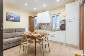 A modern kitchen with white cabinets, a dining table with chairs, and a sofa in a living area.