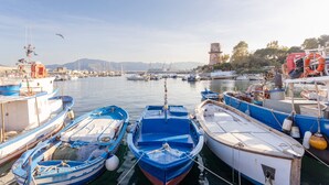 Un puerto deportivo con varias embarcaciones amarradas, un faro y montañas al fondo.
