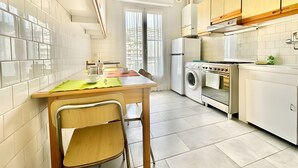 A modern kitchen with white appliances, a dining area with a table and chairs, and a large window with curtains. - Apartment 'Flaminia' with Balcony and Wi-Fi (Sanremo)