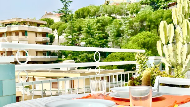 A table set outdoors with plates, cutlery, and a glass, overlooking a residential area with buildings and greenery. - Apartment 'Flaminia' with Balcony and Wi-Fi (Sanremo)