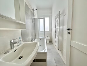 Ein modernes Badezimmer mit Badewanne, Dusche und Waschbecken, ausgestattet mit weißen Armaturen und einem Fliesenboden.
