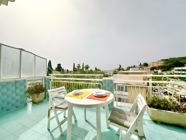 Ein Balkon mit rundem Tisch und Stühlen, Blumentöpfen und Blick auf die Stadt.