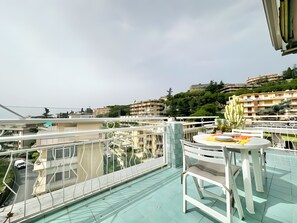 Ein Balkon mit Tisch und Stühlen, einem Geländer und Blick auf Gebäude und Grünflächen.
