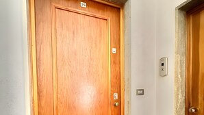 A wooden door with a number plate, a wall-mounted light switch, and a stone floor. - Apartment 'Flaminia' with Balcony and Wi-Fi (Sanremo)