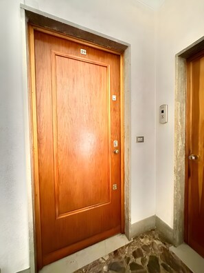 Eine Holztür mit einer Nummernschild und einem Wandlichtschalter, außerdem ein Steinfußboden.