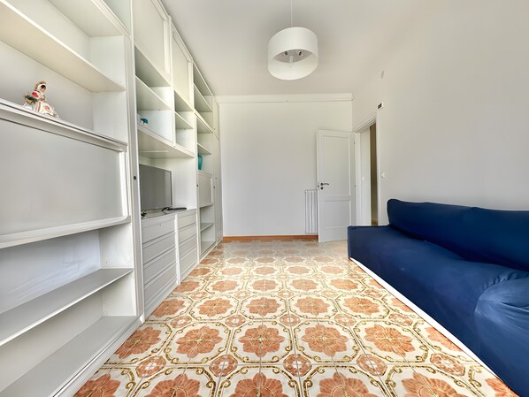A room with a blue sofa, a white wardrobe, and patterned floor tiles.