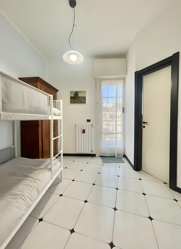 Una habitación con literas, una puerta, un radiador y una ventana con cortinas.