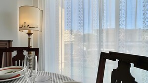 Un comedor con mantel a cuadros, una lámpara de mesa y vistas a través de cortinas de encaje.