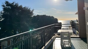Un balcón con vista al mar, barandilla y una mesa con una silla.