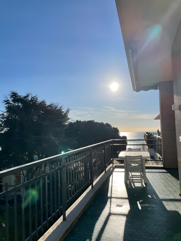 A balcony with a view of the sea, a railing, and a table with a chair.