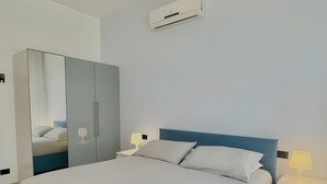 Una habitación de hotel moderna con una cama grande, un armario, una mesita de noche con lámpara y un equipo de aire acondicionado.