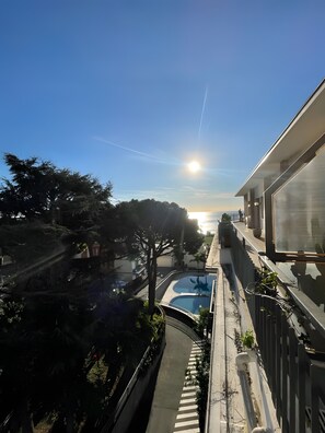 A rooftop pool with a clear view of the sunset, surrounded by trees and a modern building structure.