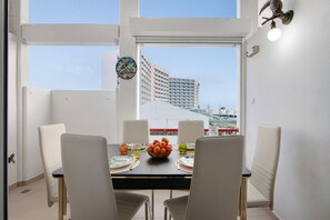 Un comedor con una mesa dispuesta para cuatro, un frutero y vistas a un edificio a través de amplias ventanas.