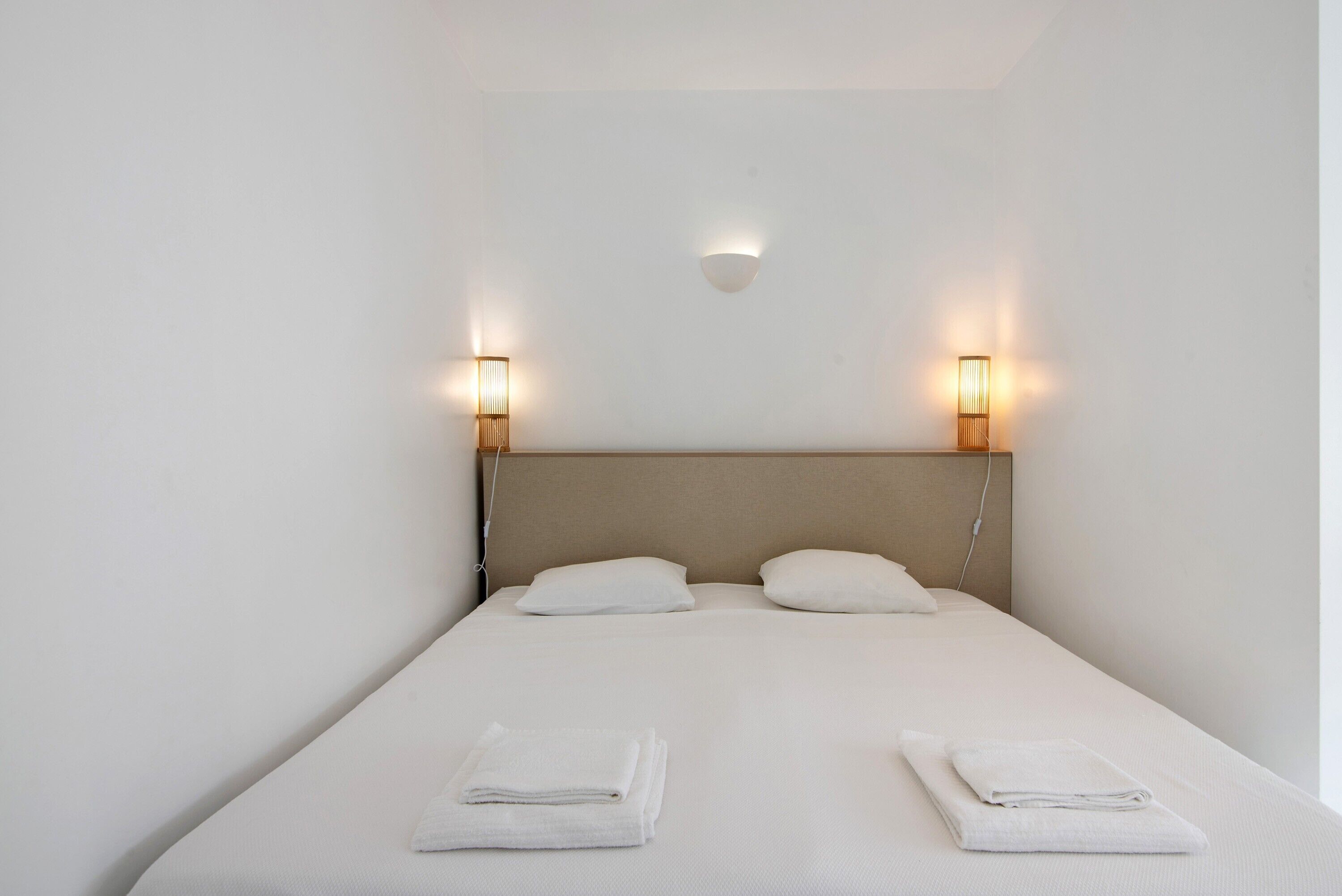 Una cama individual con dos almohadas, dos lámparas de noche y dos toallas dobladas.