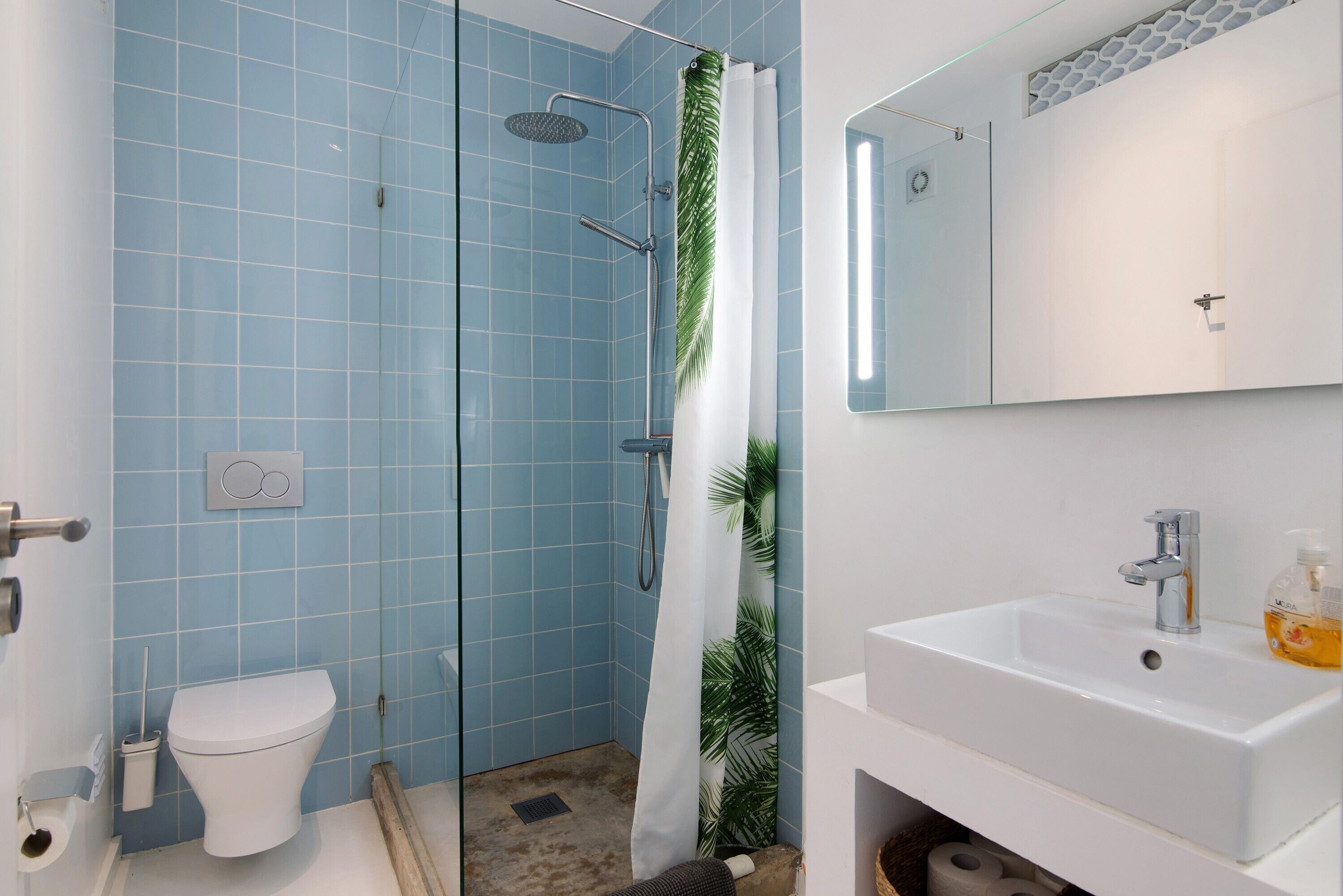 A bathroom with a toilet, shower, sink, and mirror.