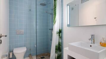 A bathroom with a toilet, shower, sink, and mirror.