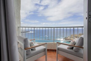 Un balcon avec vue sur l’océan, des fauteuils blancs avec des coussins et une balustrade.