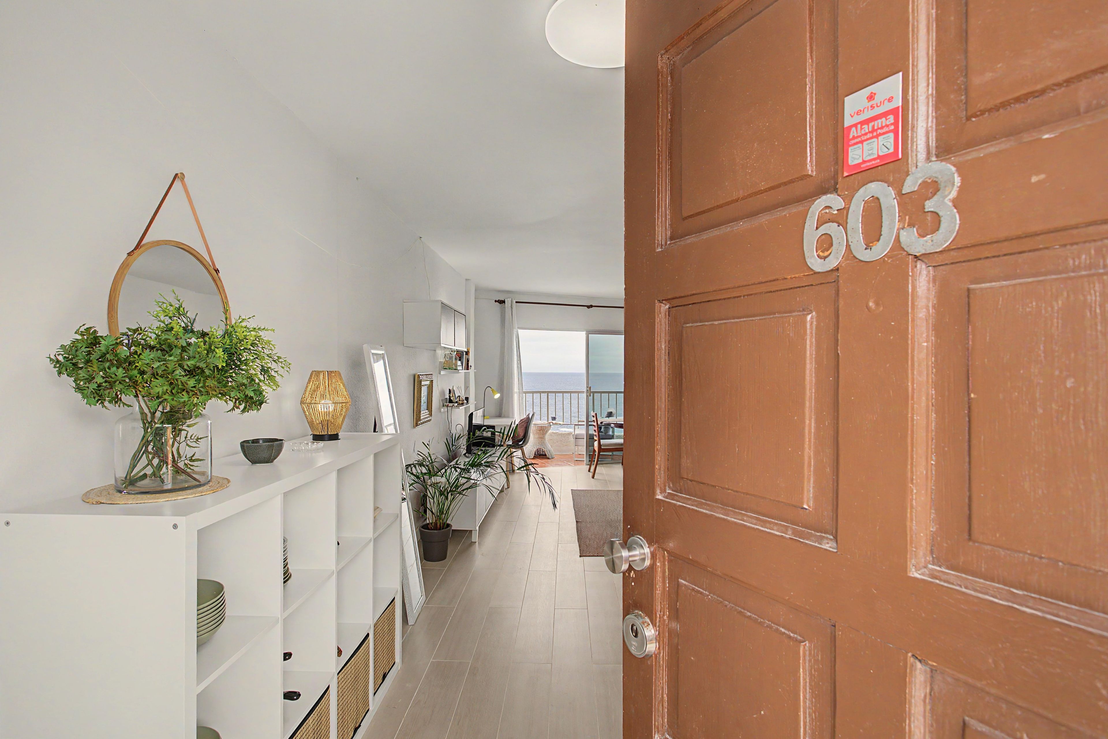 Un couloir avec une porte en bois portant l’inscription « 603 » et une étagère blanche ornée d’objets décoratifs.