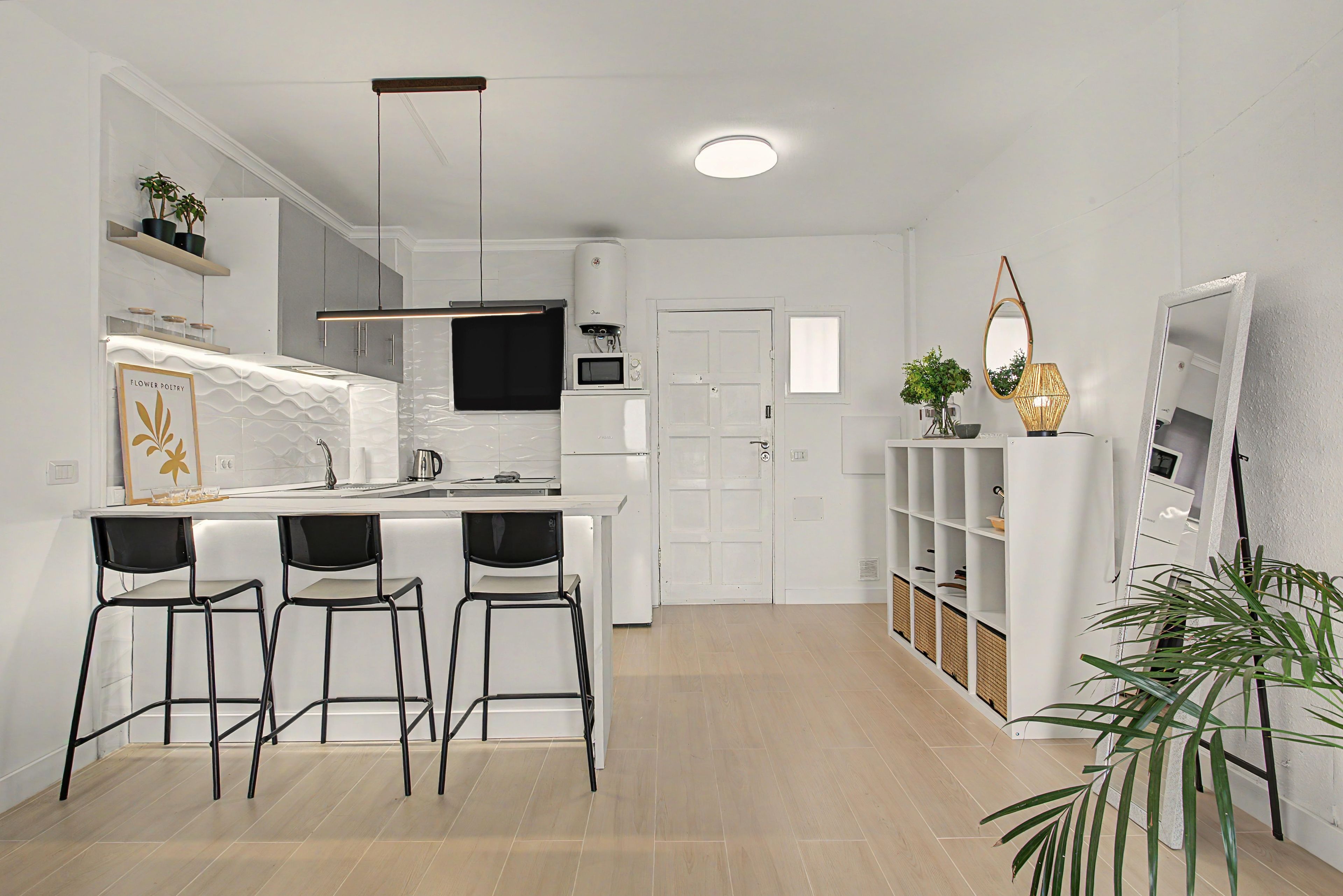 Una cocina moderna con barra, armarios blancos y televisor de pantalla plana.