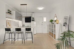 A modern kitchen with a bar area, white cabinetry, and a flat-screen TV.