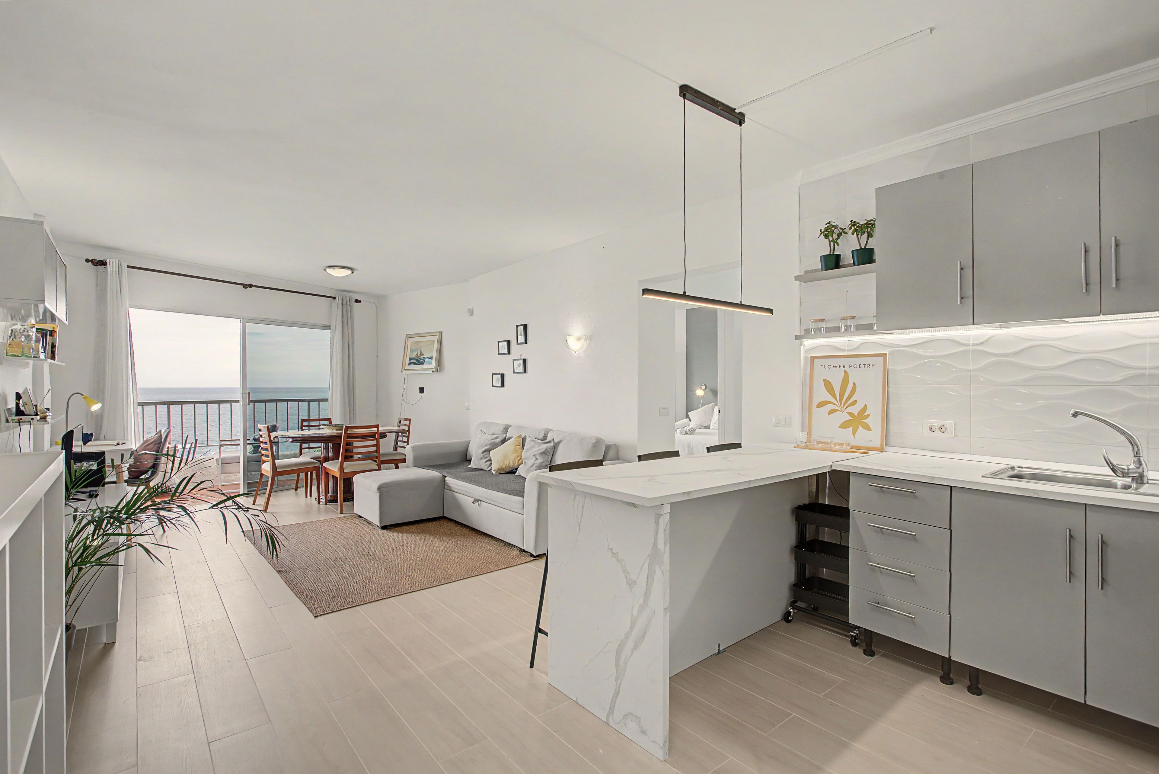 A modern kitchen with a marble countertop, grey cabinets, and a view to the outside.