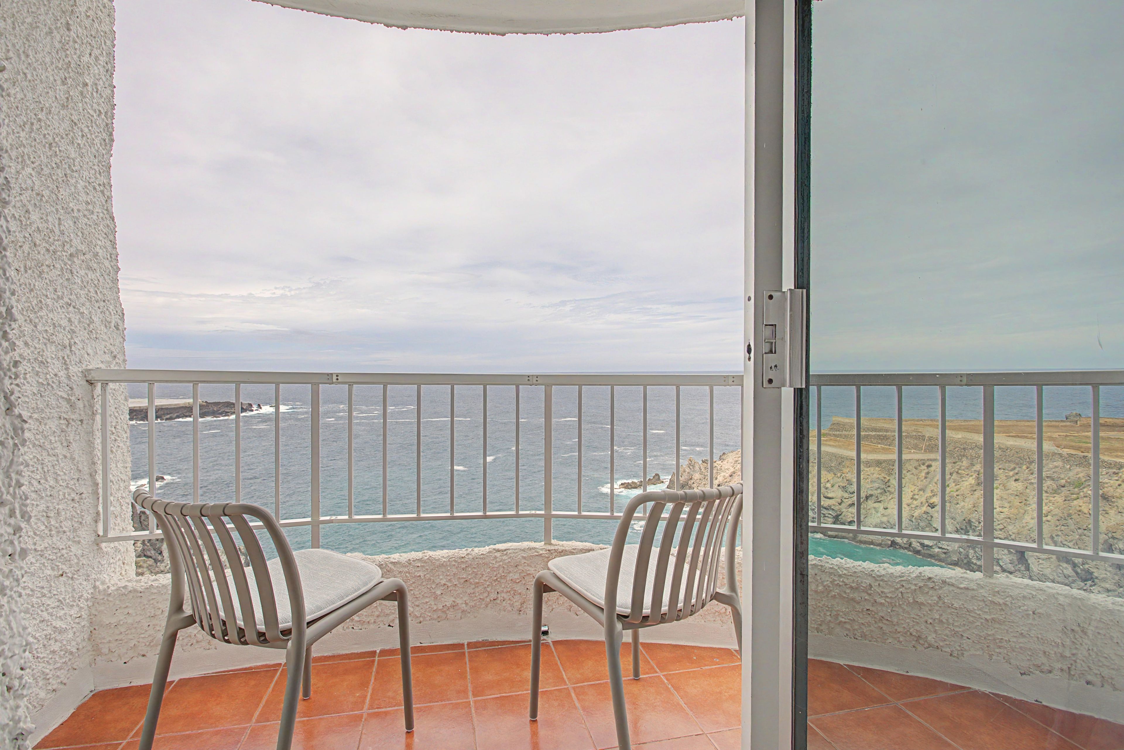 Un balcon avec deux chaises, une vue sur la mer et une côte rocheuse.