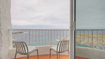 Un balcon avec deux chaises, une vue sur la mer et une côte rocheuse.