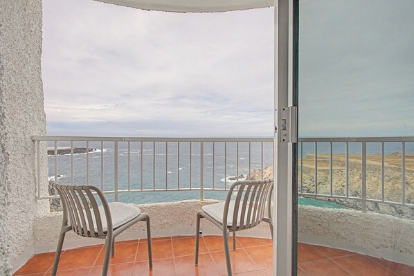 A balcony with two chairs, a view of the sea, and a rocky coastline.