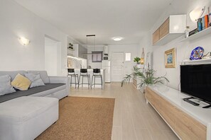 Ein modernes Wohnzimmer mit einer Couch, einem Fernseher und einer Küche im Hintergrund.