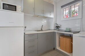 Una cocina compacta con microondas, lavamanos y armarios.