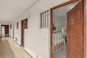 Ein Korridor mit zum Zimmer führenden Türen, einer weißen Wand und einem gefliesten Boden.