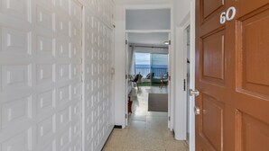Un pasillo con una pared blanca con diseño, una puerta de madera con el número 60, y vista a un balcón con barandilla.