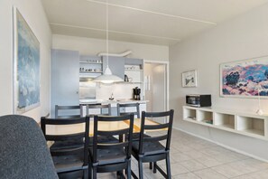 A modern kitchen with white cabinets, a dining table with chairs, a hanging light fixture, and a painting on the wall. - Holiday apartment near Bønnerup (Glesborg)