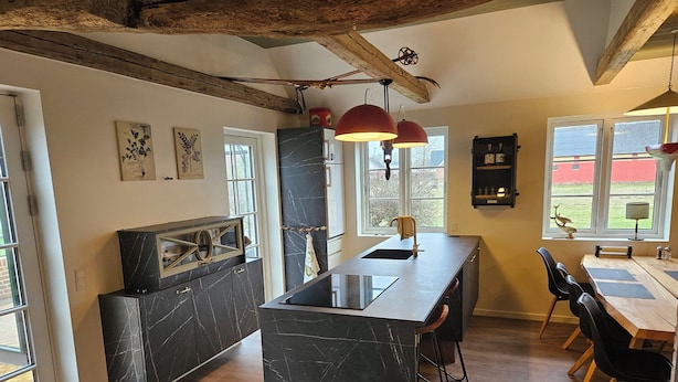 Een moderne keuken met een marmeren eiland, houten balken en grote ramen.