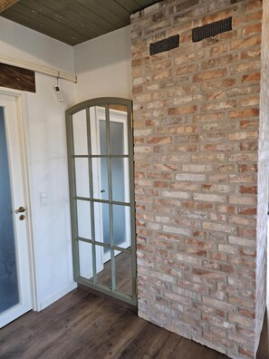 A room with a wooden ceiling, a brick wall, a white door with a glass panel, and a wooden floor.