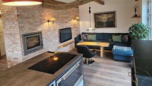 Een moderne woonkamer met met bakstenen muren, een open haard, een flatscreen televisie, een eettafel en een blauwe bank.