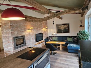 A modern living room with exposed brick walls, a fireplace, a flat-screen TV, a dining table, and a blue sofa.
