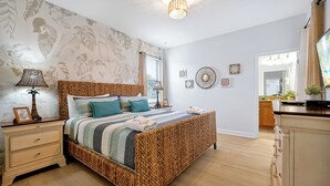 A bedroom with a large bed, a nightstand, a lamp, and a wall with framed pictures.