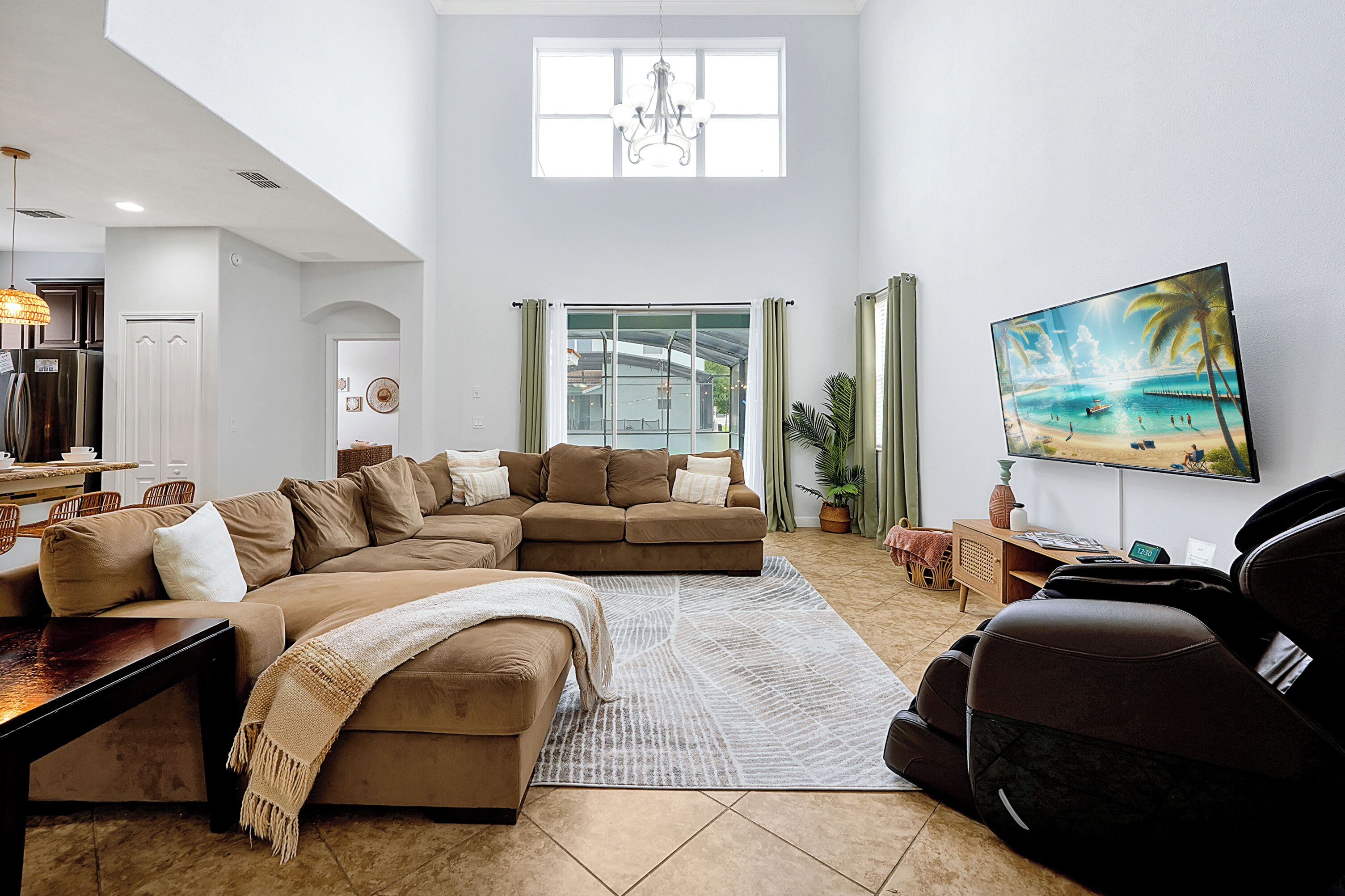 A spacious living room with a sectional sofa, a flat-screen TV, and a large window offering a view of the outdoors.