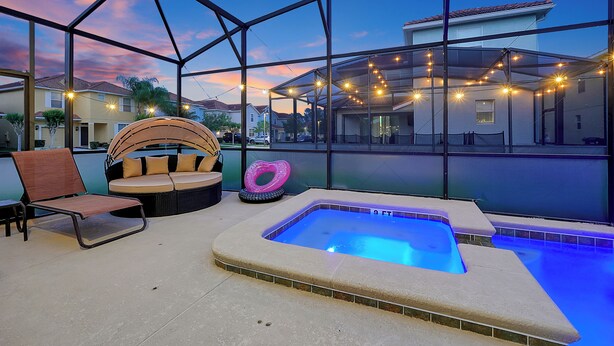 A covered outdoor area with a hot tub, lounge chairs, and string lights.