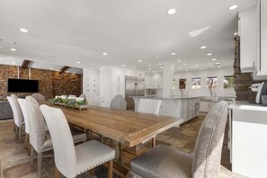 A spacious kitchen with white cabinets, a wooden dining table, and a stone accent wall.