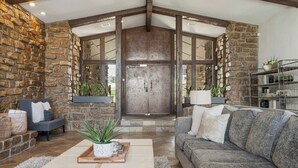 A spacious living area with a stone wall, a large wooden door, a grey sofa, and a coffee table with a plant. - Grotto @ Southern Hills W/Pool & Hot Tub (Tulsa)
