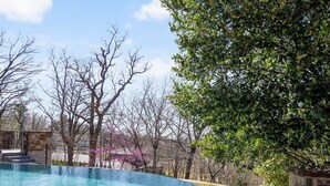A swimming pool with clear water, surrounded by stone steps and a tree. - Grotto @ Southern Hills W/Pool & Hot Tub (Tulsa)