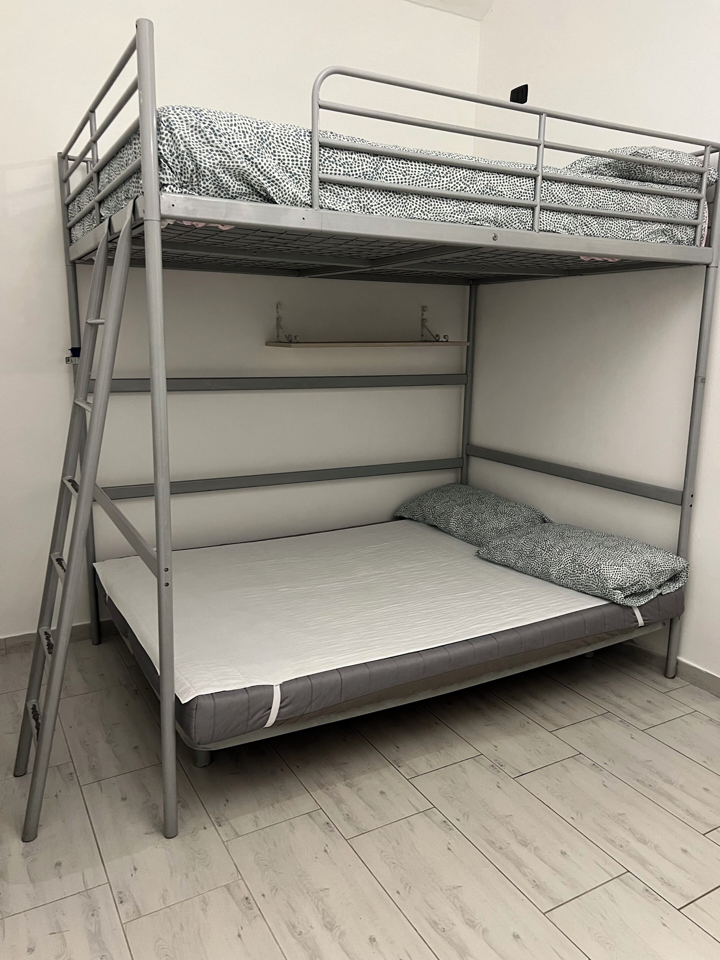A bunk bed with a ladder, a shelf above the top bunk, and a mattress with a patterned cover.