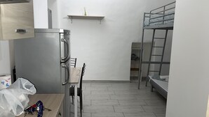 A compact room with a kitchenette, a bunk bed, a small table, and a chair. - Bed2Go Brescia (Turin)